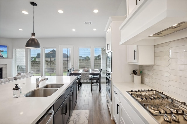 kitchen with tasteful backsplash, pendant lighting, white cabinets, sink, and custom range hood