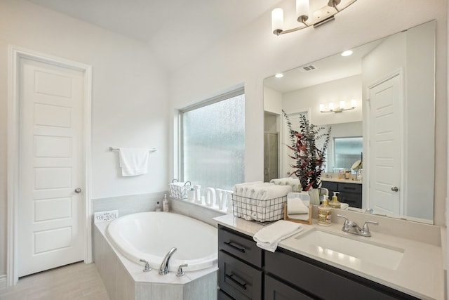 bathroom with a relaxing tiled tub, tile patterned floors, and vanity