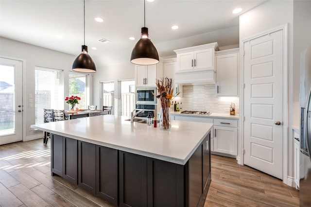 kitchen featuring white cabinetry, decorative light fixtures, stainless steel appliances, and an island with sink