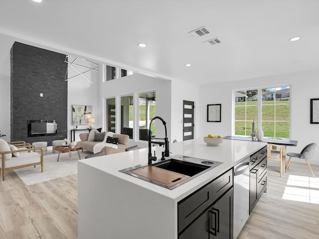 kitchen with sink, a fireplace, light wood-type flooring, and a kitchen island with sink