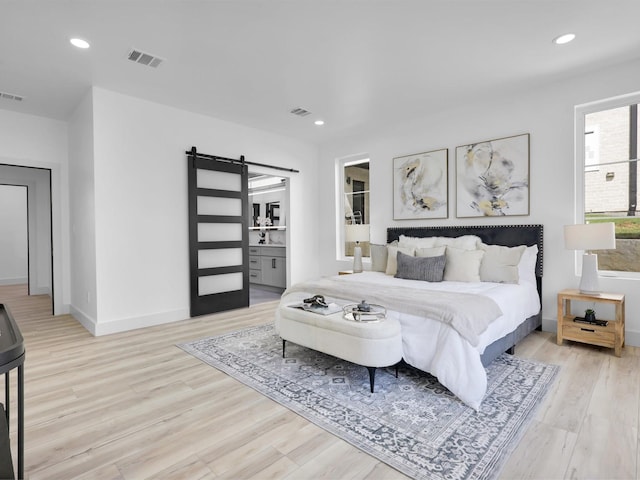 bedroom with ensuite bathroom, light hardwood / wood-style flooring, and a barn door