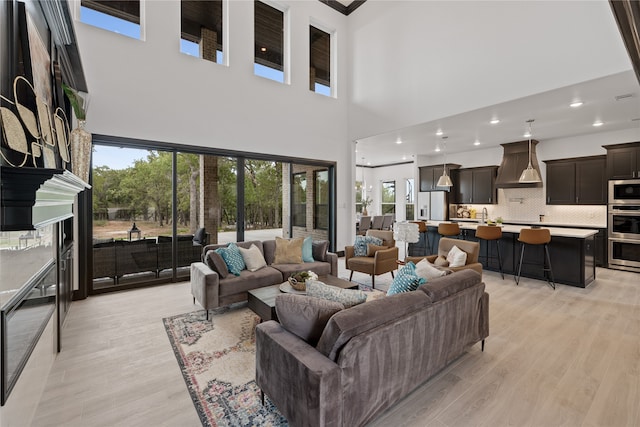 living room with a high ceiling, sink, light wood-type flooring, and a large fireplace