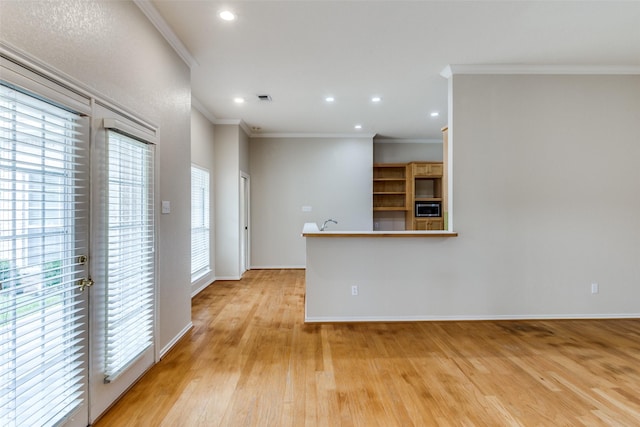 kitchen with stainless steel microwave, ornamental molding, and light hardwood / wood-style floors