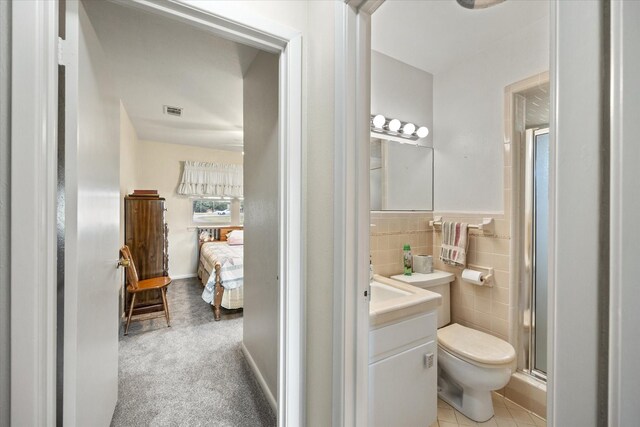 bathroom with tile patterned flooring, a shower with shower door, toilet, vanity, and tile walls