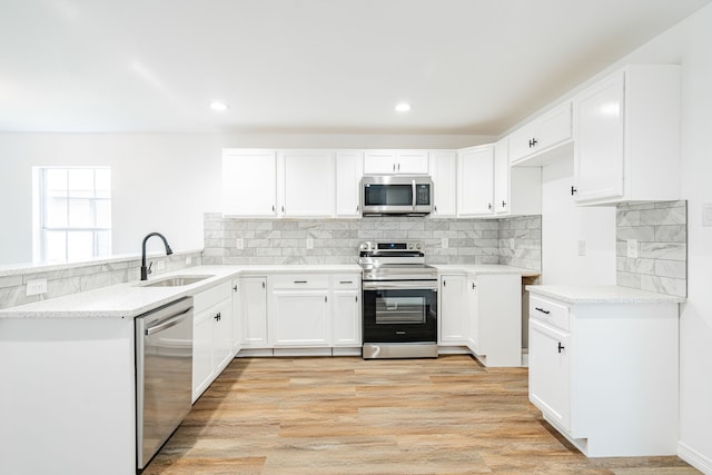 kitchen with sink, white cabinetry, light stone counters, light wood-type flooring, and appliances with stainless steel finishes