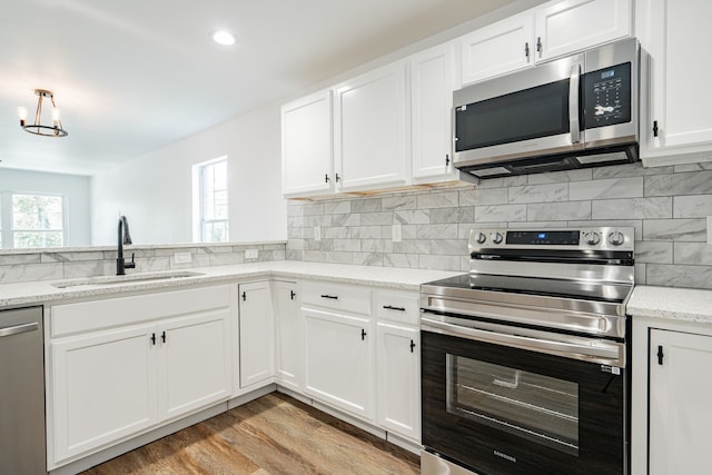 kitchen featuring sink, appliances with stainless steel finishes, white cabinetry, light stone counters, and decorative backsplash