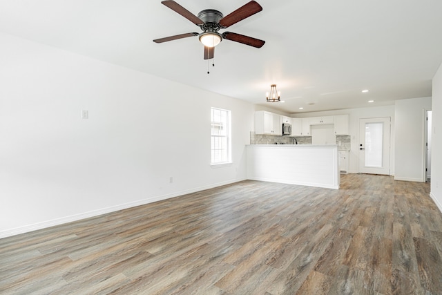 unfurnished living room featuring ceiling fan with notable chandelier and light wood-type flooring