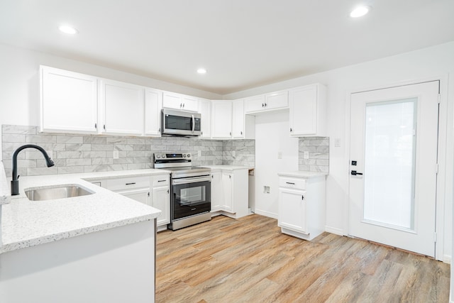 kitchen featuring appliances with stainless steel finishes, sink, white cabinets, light stone counters, and light hardwood / wood-style floors