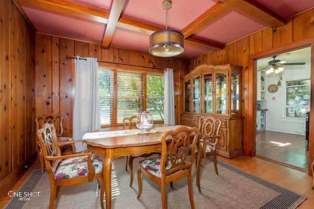 dining room featuring wood walls, beam ceiling, coffered ceiling, and light wood-type flooring