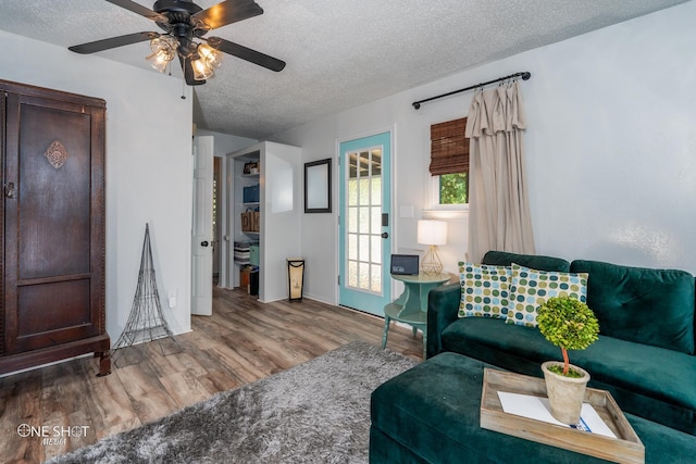 living room with a textured ceiling, ceiling fan, and wood-type flooring