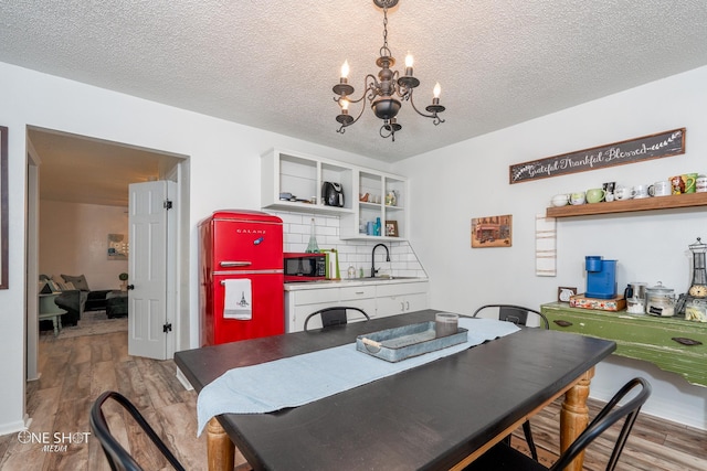 dining area with a textured ceiling, sink, an inviting chandelier, and wood-type flooring