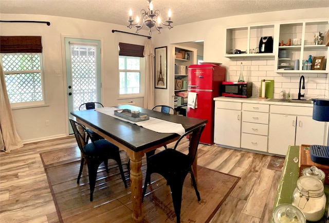 dining room featuring sink, a textured ceiling, a notable chandelier, and light hardwood / wood-style floors