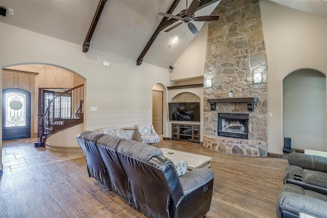 living room with ceiling fan, a stone fireplace, beamed ceiling, high vaulted ceiling, and a textured ceiling