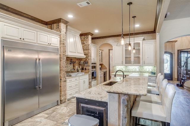 kitchen with light stone countertops, sink, stainless steel appliances, an island with sink, and decorative light fixtures