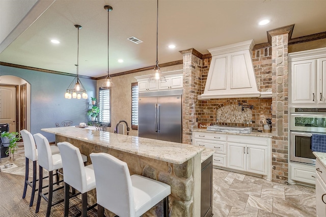 kitchen with appliances with stainless steel finishes, light stone counters, pendant lighting, and an island with sink