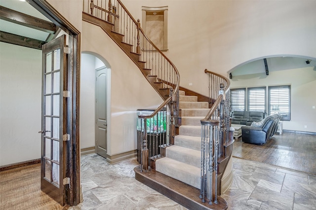 staircase featuring beamed ceiling, wood-type flooring, and a towering ceiling