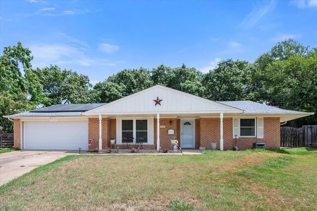 single story home with a garage, a front lawn, solar panels, and covered porch