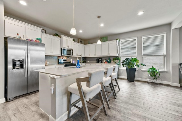 kitchen with pendant lighting, white cabinets, a center island with sink, light hardwood / wood-style floors, and stainless steel appliances