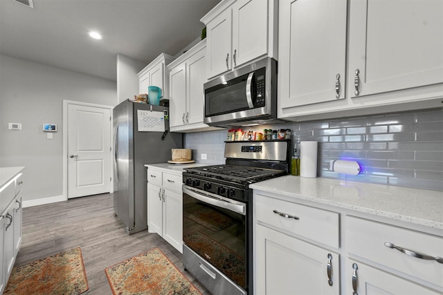 kitchen featuring backsplash, light stone counters, stainless steel appliances, white cabinets, and light hardwood / wood-style floors