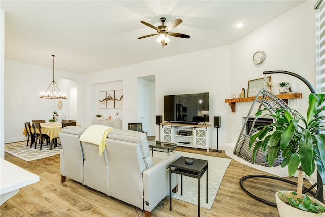 living room with a fireplace, ceiling fan with notable chandelier, and light wood-type flooring