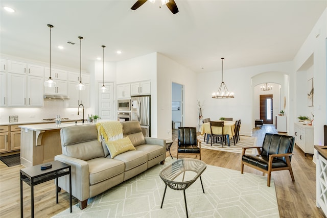 living room with light wood-type flooring and ceiling fan with notable chandelier