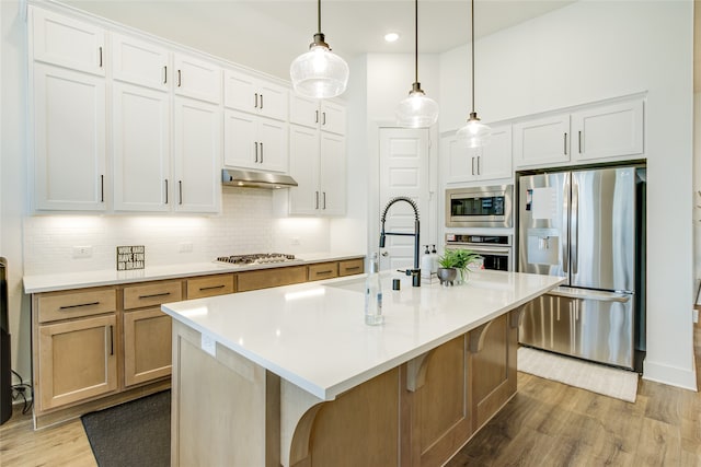 kitchen featuring white cabinets, light hardwood / wood-style floors, appliances with stainless steel finishes, and a center island with sink