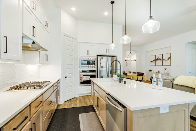 kitchen featuring stainless steel appliances, white cabinets, a center island with sink, light hardwood / wood-style floors, and backsplash