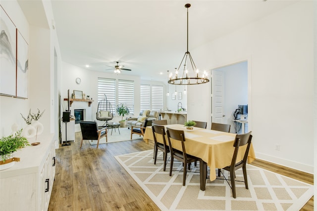 dining area with light wood-type flooring and ceiling fan with notable chandelier