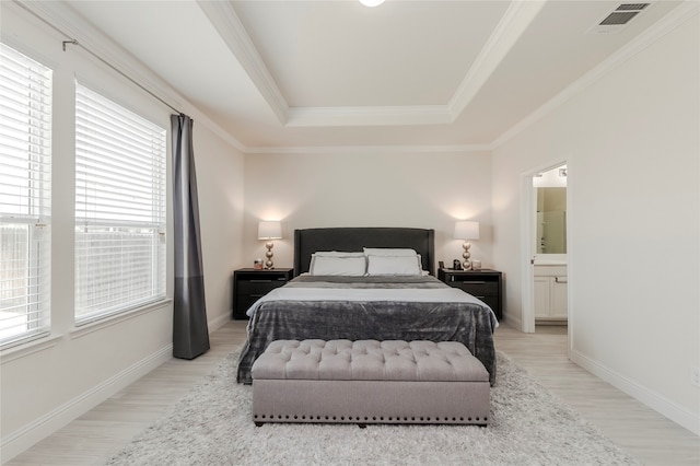 bedroom featuring multiple windows, light hardwood / wood-style flooring, a tray ceiling, and connected bathroom