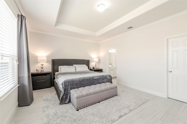 bedroom with light hardwood / wood-style floors, connected bathroom, ornamental molding, and a tray ceiling