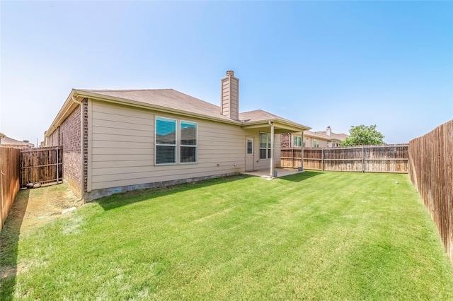 back of property featuring brick siding, a chimney, a fenced backyard, and a lawn