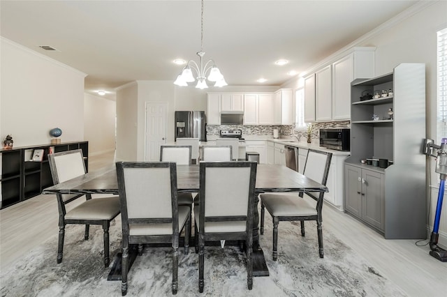 dining room with light wood-style flooring, visible vents, and ornamental molding