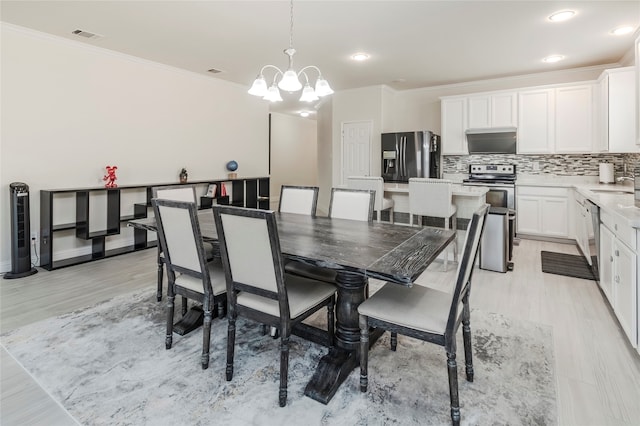 dining room with sink, light hardwood / wood-style flooring, an inviting chandelier, and crown molding