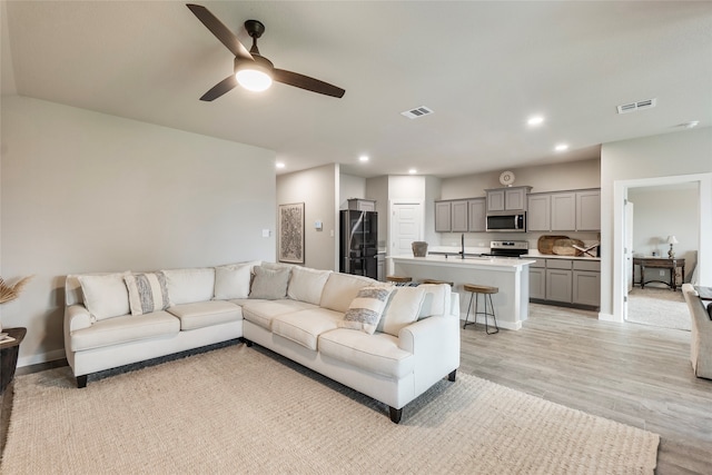 living room featuring sink, ceiling fan, and light wood-type flooring