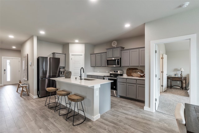 kitchen featuring sink, light colored carpet, appliances with stainless steel finishes, a kitchen breakfast bar, and a kitchen island with sink