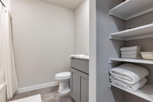 bathroom with toilet, wood finished floors, vanity, baseboards, and shower / tub combo with curtain