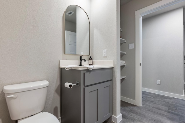 half bath featuring a textured wall, toilet, wood finished floors, vanity, and baseboards