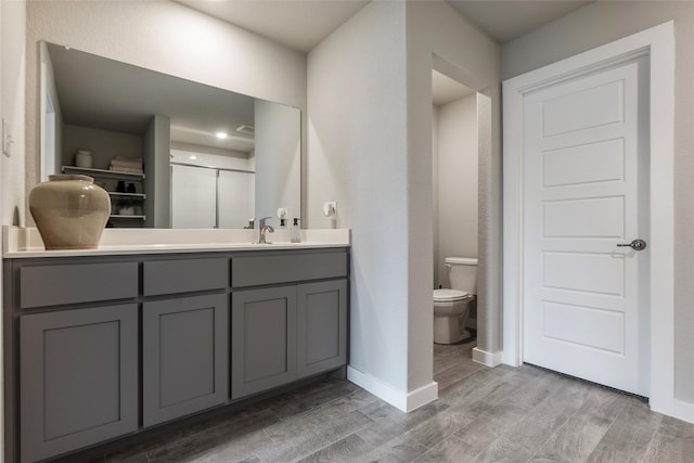 bathroom with baseboards, toilet, wood finished floors, vanity, and a shower stall