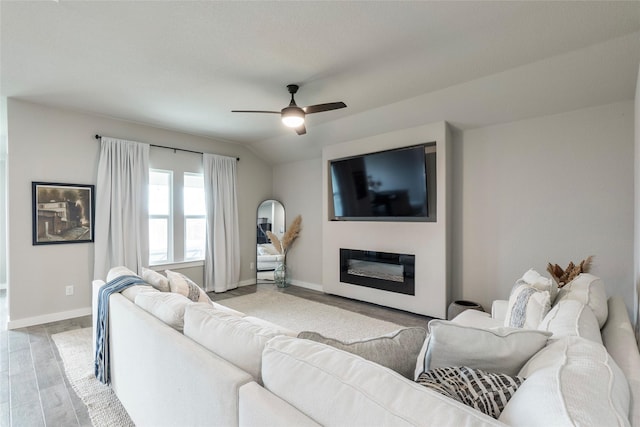 living room featuring lofted ceiling, a ceiling fan, baseboards, light wood-type flooring, and a glass covered fireplace