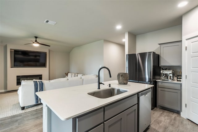 kitchen featuring sink, appliances with stainless steel finishes, gray cabinets, and an island with sink