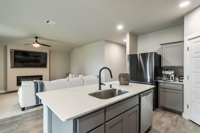 kitchen featuring an island with sink, appliances with stainless steel finishes, open floor plan, light countertops, and a sink