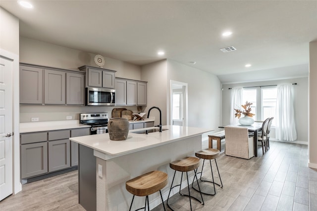 kitchen with gray cabinets, appliances with stainless steel finishes, light wood-type flooring, and an island with sink