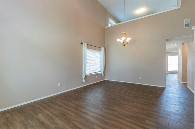 empty room featuring a towering ceiling, dark hardwood / wood-style flooring, and a notable chandelier