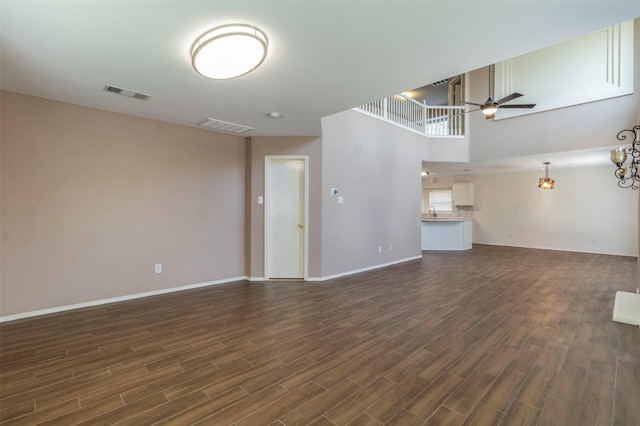 unfurnished living room featuring ceiling fan, dark hardwood / wood-style flooring, a towering ceiling, and sink