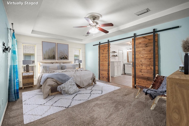 carpeted bedroom featuring multiple windows, a barn door, a raised ceiling, and ensuite bathroom