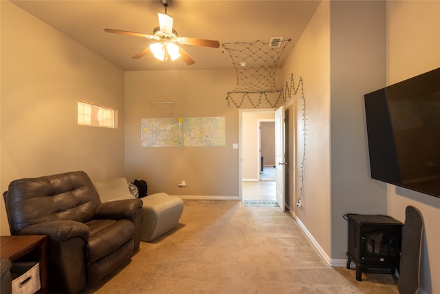 sitting room featuring light carpet, ceiling fan, and a wood stove