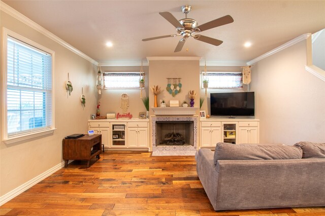 living room with a high end fireplace, ceiling fan, light hardwood / wood-style flooring, and ornamental molding