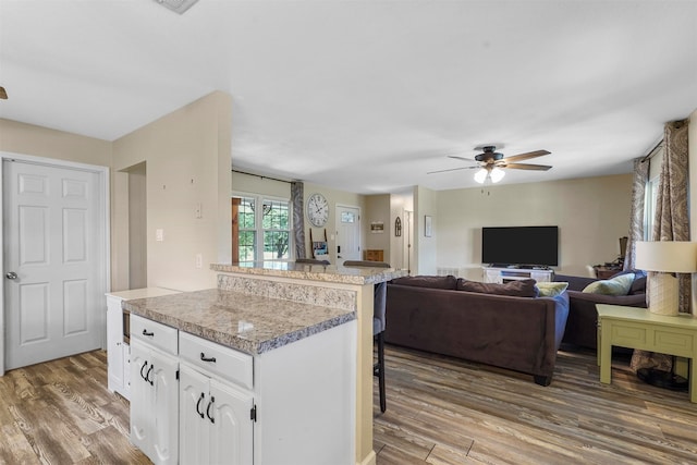 kitchen featuring a kitchen bar, white cabinets, a center island, ceiling fan, and wood-type flooring