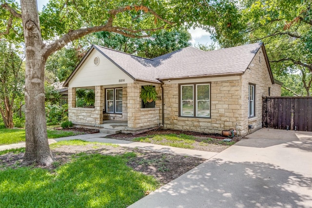 view of front of home featuring stone siding, roof with shingles, and fence