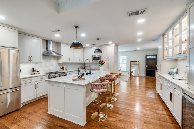 kitchen with white cabinetry, light wood-type flooring, wall chimney range hood, and stainless steel appliances